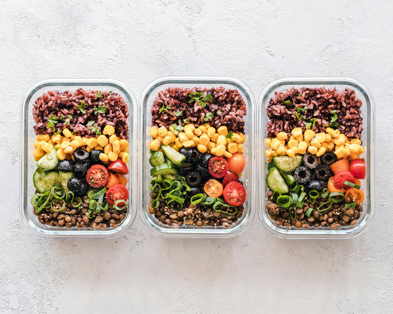 about-02 Colorful healthy meal prep with corn, olives, tomatoes, and lentils in glass containers. Perfect for mindful eating.