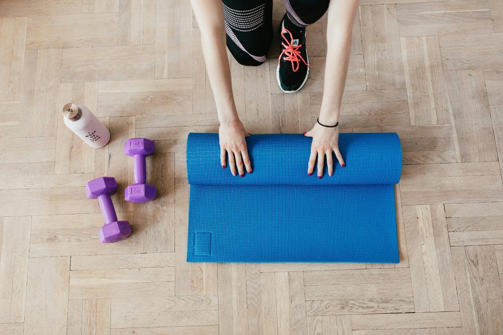 Simple home gym setup showing resistance bands, dumbbells, and a yoga mat arranged on hardwood flooring.