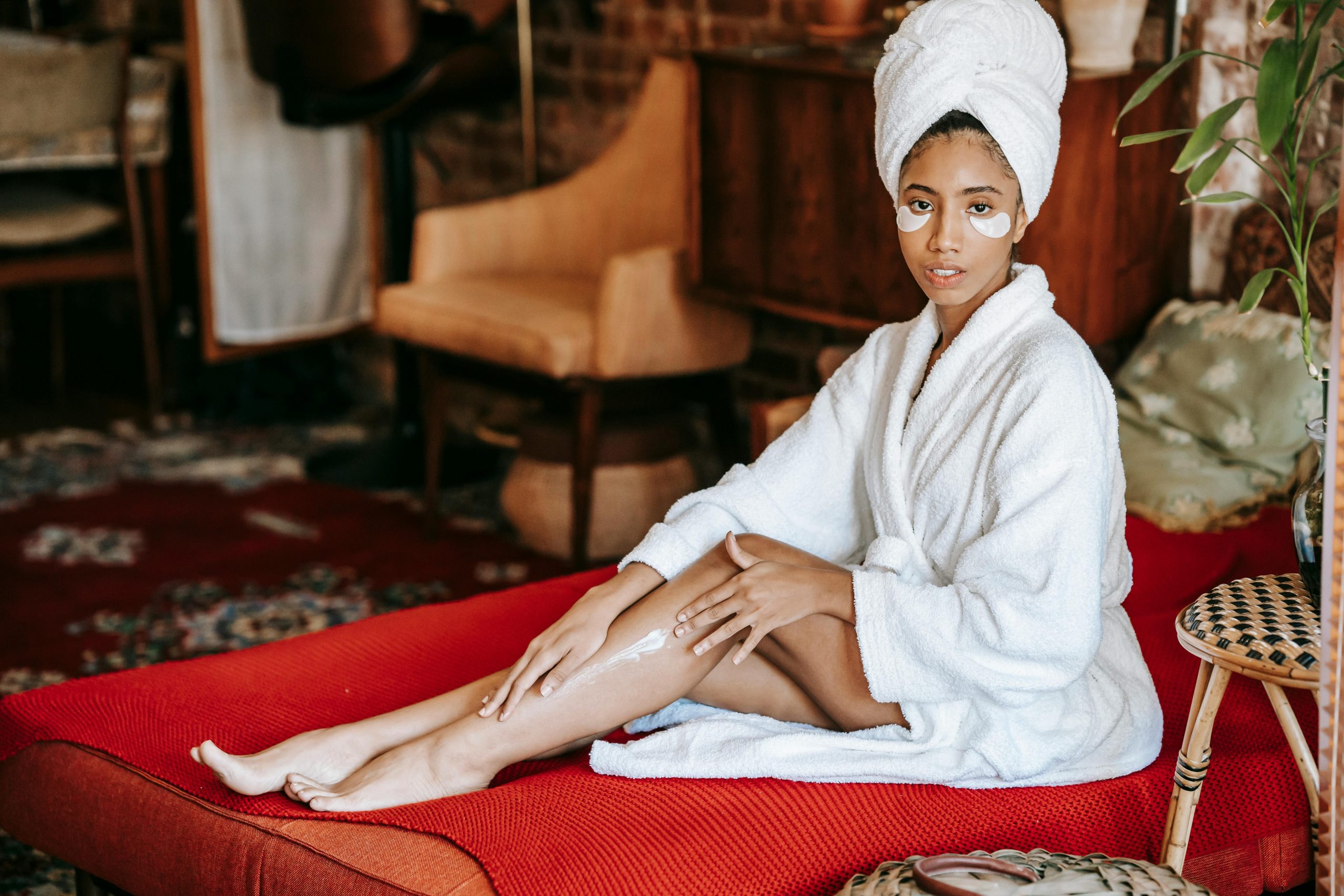 Young woman in bathrobe with skincare cream, relaxing indoors, promoting wellness and comfort.