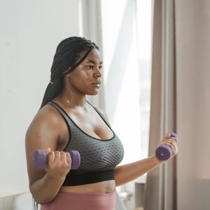 Curvy woman with braided hair working out with dumbbells indoors, embracing body positivity.
