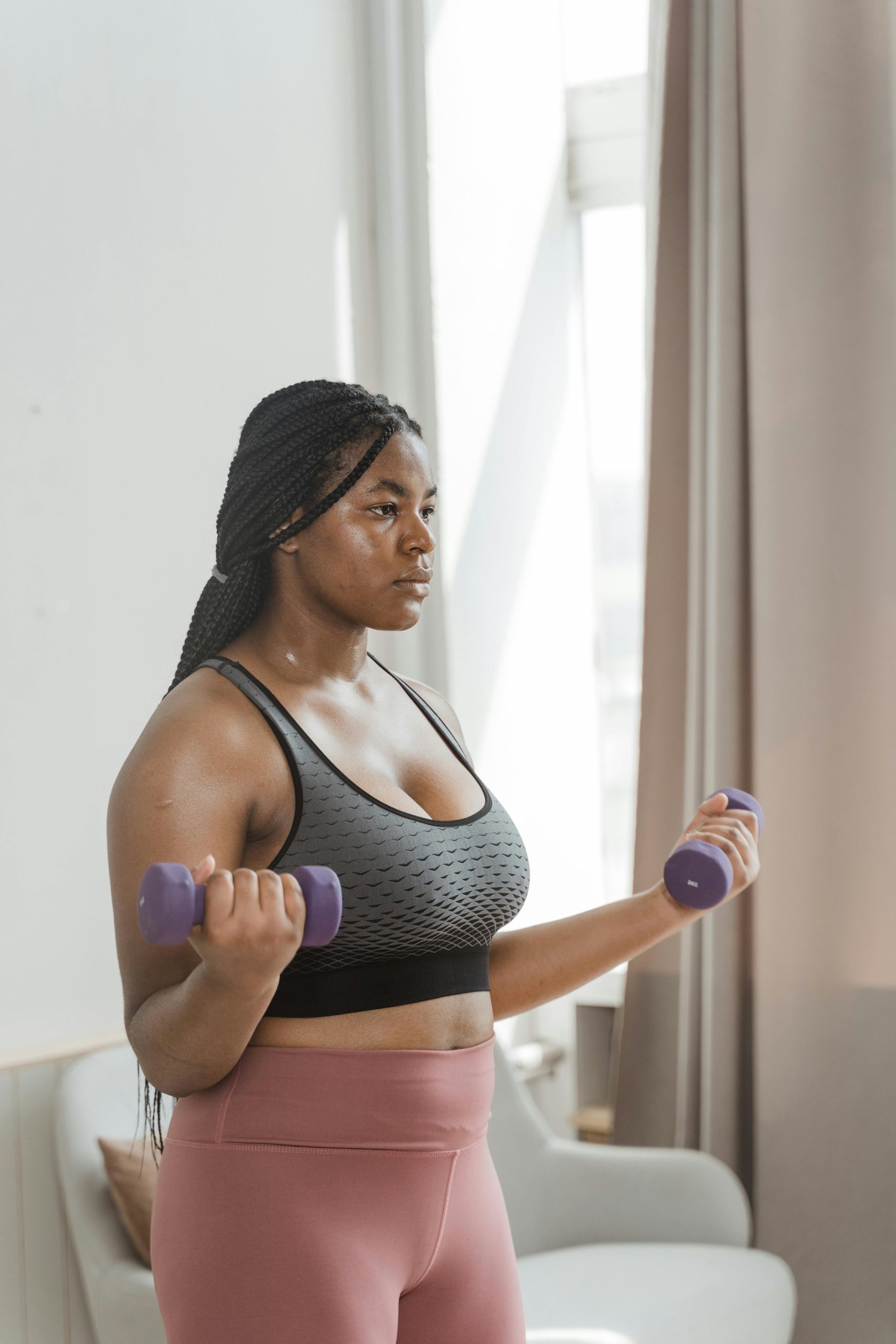 pexels-photo-8846565-8846565 Curvy woman with braided hair working out with dumbbells indoors, embracing body positivity.